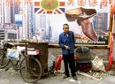 A Chinese man who makes a living selling baked sweet potatoes from a makeshift oven on his bicycle stands below a billboard which promotes shoes imported from the U.S., at a shoe market in Beijing Tuesday, Sept. 11, 2001.  Members of the World Trade Organization are meeting in Geneva this week in a bid to solve the final issues blocking China's  15-year bid to join the body which sets rules for international trade. (AP Photo/Greg Baker)