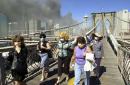 Women wearing dust masks flee across the Brooklyn  Bridge from Manhattan to Brooklyn following the collapse of both World Trade Center towers Tuesday, Sept. 11, 2001 in New York. The towers previously loomed tall in the skyline behind. (AP Photo/Mark Lennihan)