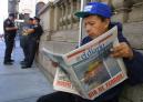 A man reads a newspaper with a front page photo of the terrorist attack on the World Trade Center, as policemen talk in the background, in New York Wednesday, Sept. 12, 2001.  Security was tightened in New York in the aftermath of the attack. (AP Photo/ Shawn Baldwin)