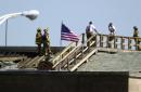 Firefighters stand along the roof of the Pentagon by an American Flag  near the damaged area of the Pentagon, Wednesday, Sept. 12, 2001. A hijacked airliner crashed into the structure on Tuesday. (AP Photo/Steve Helber)